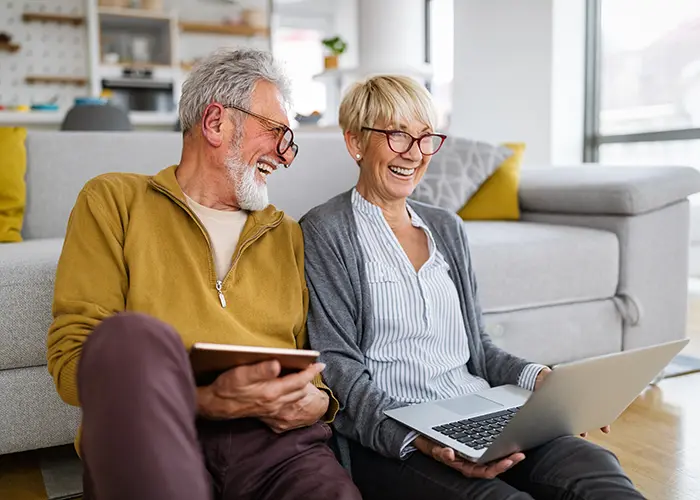 Older couple sitting in the living room with laptop, smiling and laughing