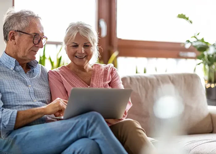 Retired couple on couch with laptop reading about annuities
