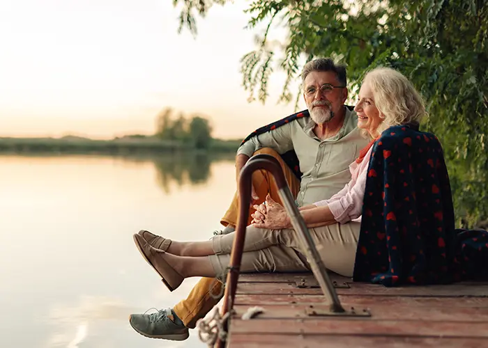 Older couple sitting on dock by lake at sunset