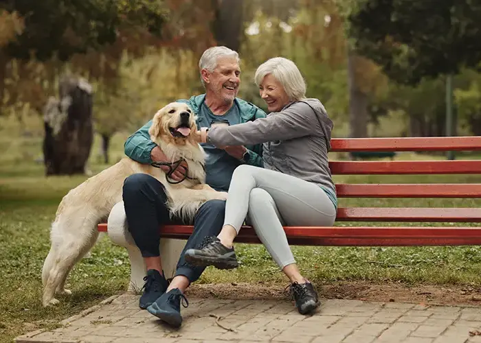 Retired couple sitting on park bench with their golden retriever